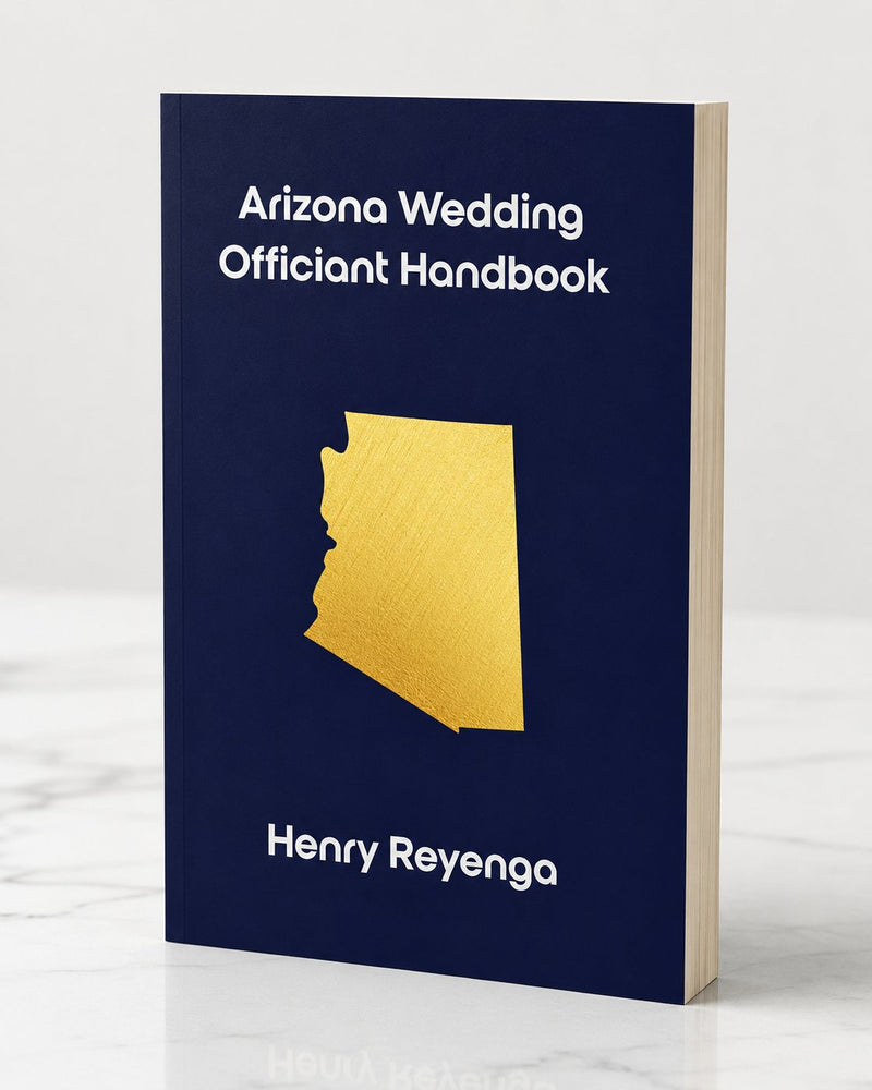 Paperback book mockup of the Arizona Wedding Officiant Handbook by Henry Reyenga standing upright on a light marble surface. The cover is dark navy blue with white text and features a gold silhouette of the state of Arizona in the center. The book has a realistic paperback spine and cream-colored page edges, photographed against a soft light gray background.