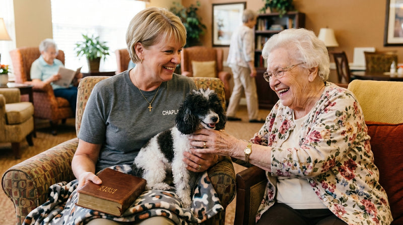 Two women sitting together with a small dog in a cozy living room setting.