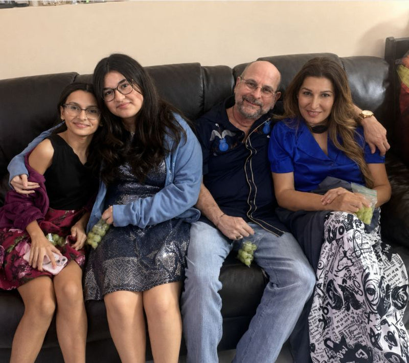Family of four sitting together on a couch with a neutral background